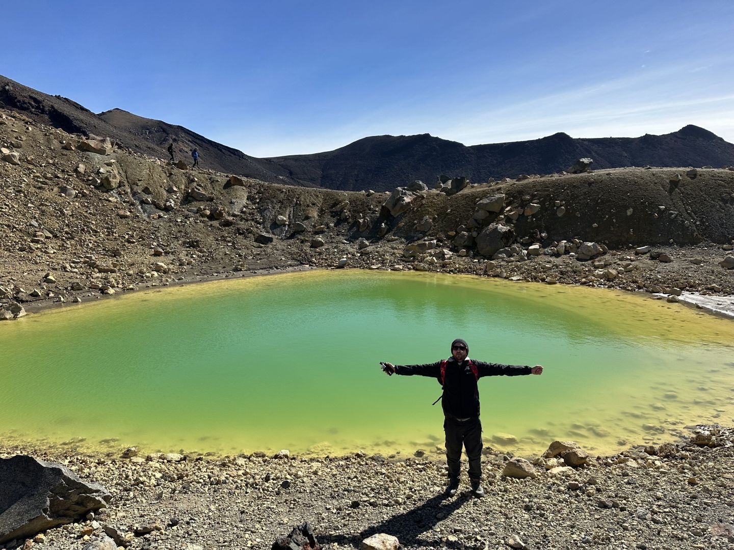 A picture of a hiker with their arms outstretched at the Emerald Lake on the Tongariro Alpine Crossing