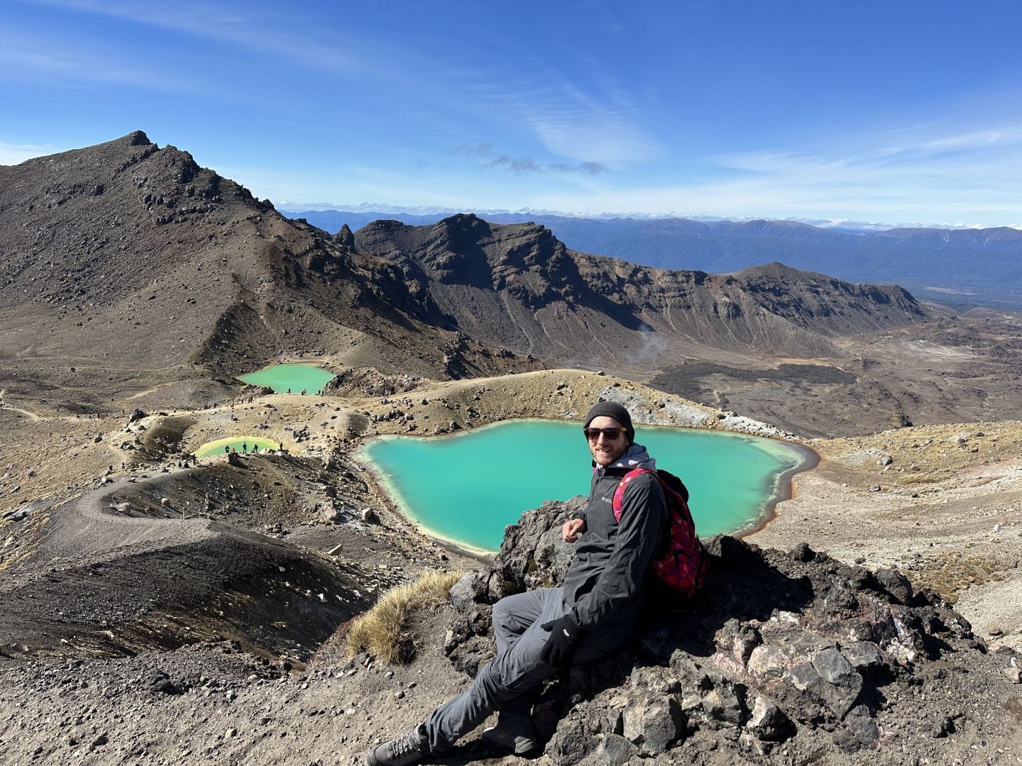 A hiker posing for a photo in front of the Emerald Lakes on the Tongariro Alpine Crossing
