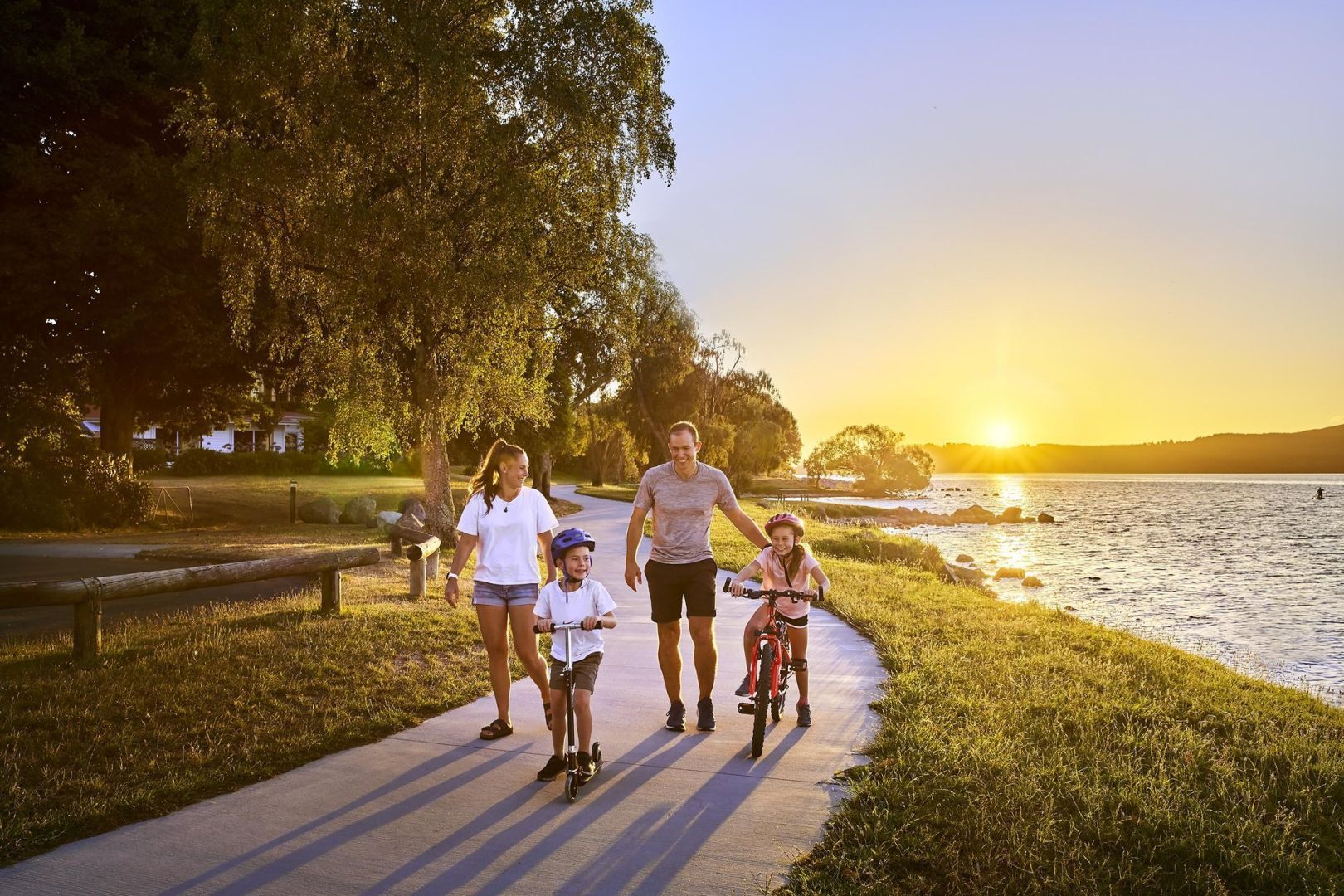 Family biking and walking along a waterfront path at sunset
