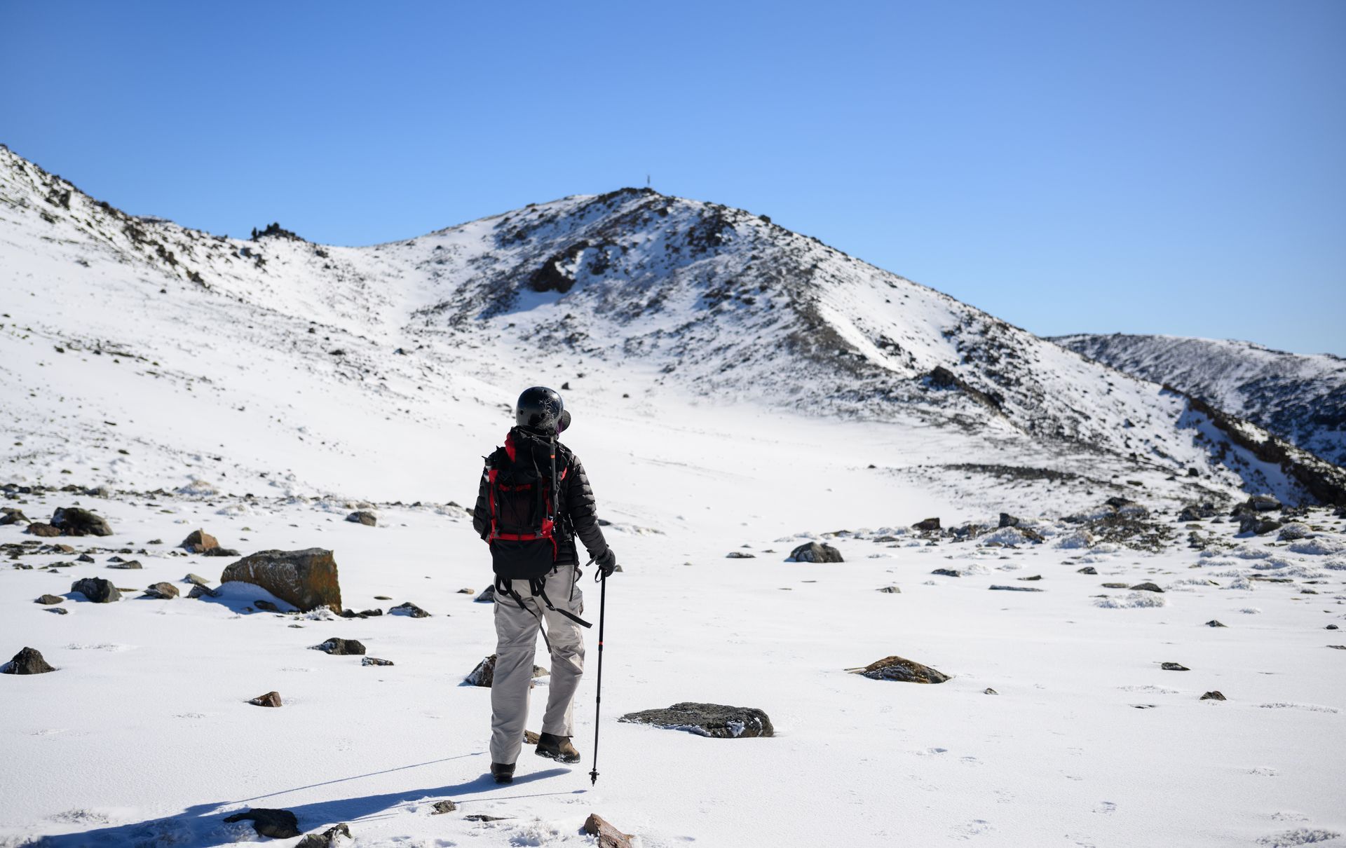 Hiker with backpack trekking through a snowy mountain landscape under a clear blue sky