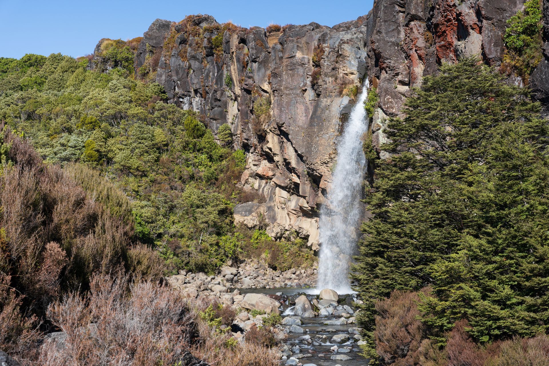 Tall waterfall cascading down a rocky cliff surrounded by green trees and shrubs