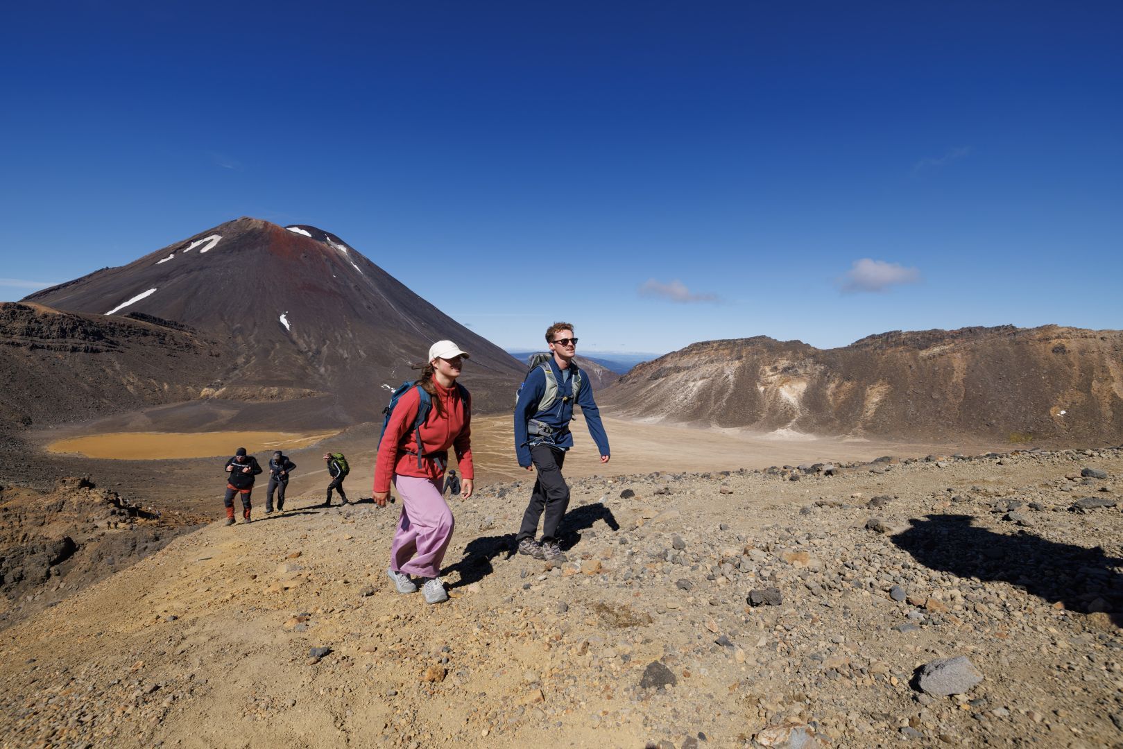 Two groups of people walking the Tongariro Alpine Crossing on a sunny day