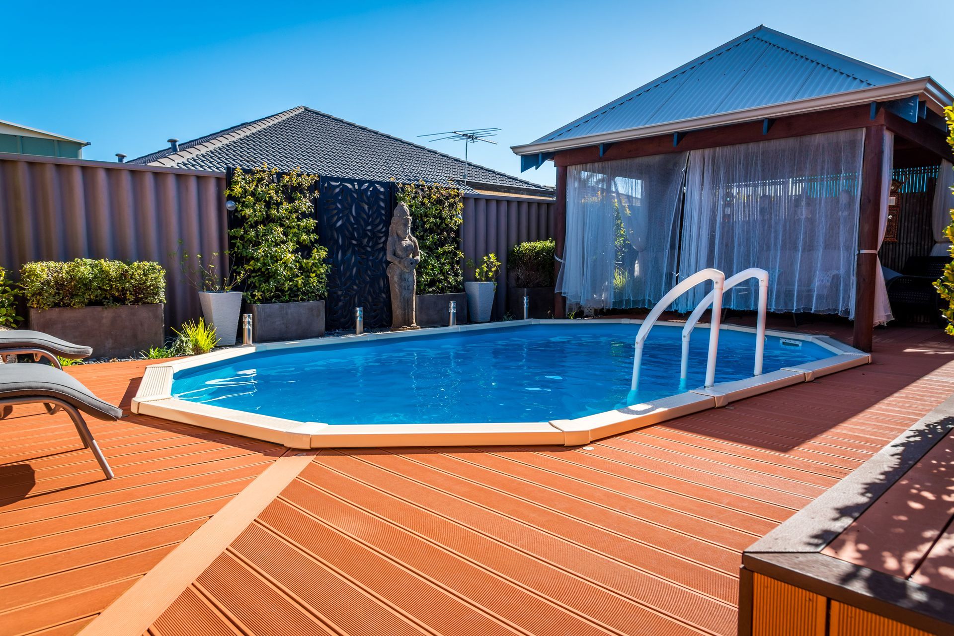 Backyard swimming pool with orange deck, blue water, and fenced patio under a clear sky