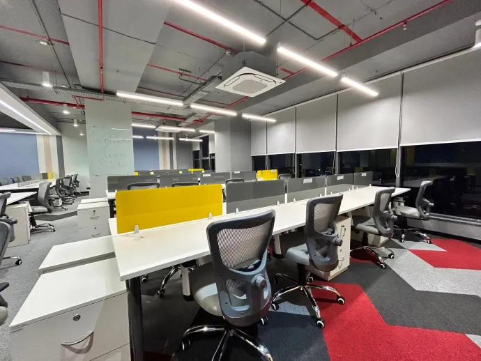 Modern open-plan office with desks, swivel chairs, and yellow divider panels under bright ceiling lights
