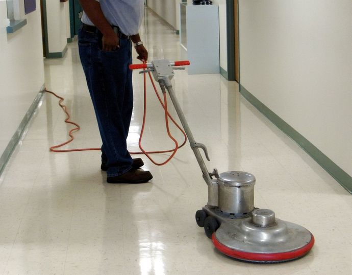 Person using a floor buffer with a red power cord in a hallway