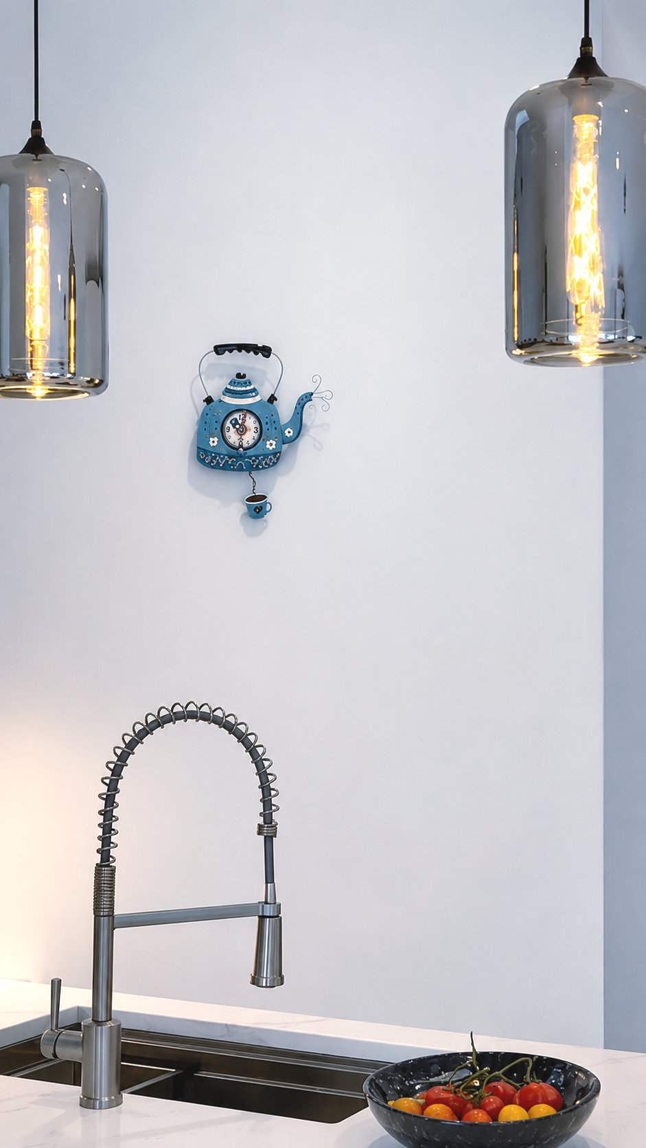 Modern kitchen sink with hanging pendant lights, blue wall decor, and a bowl of fruit on the counter