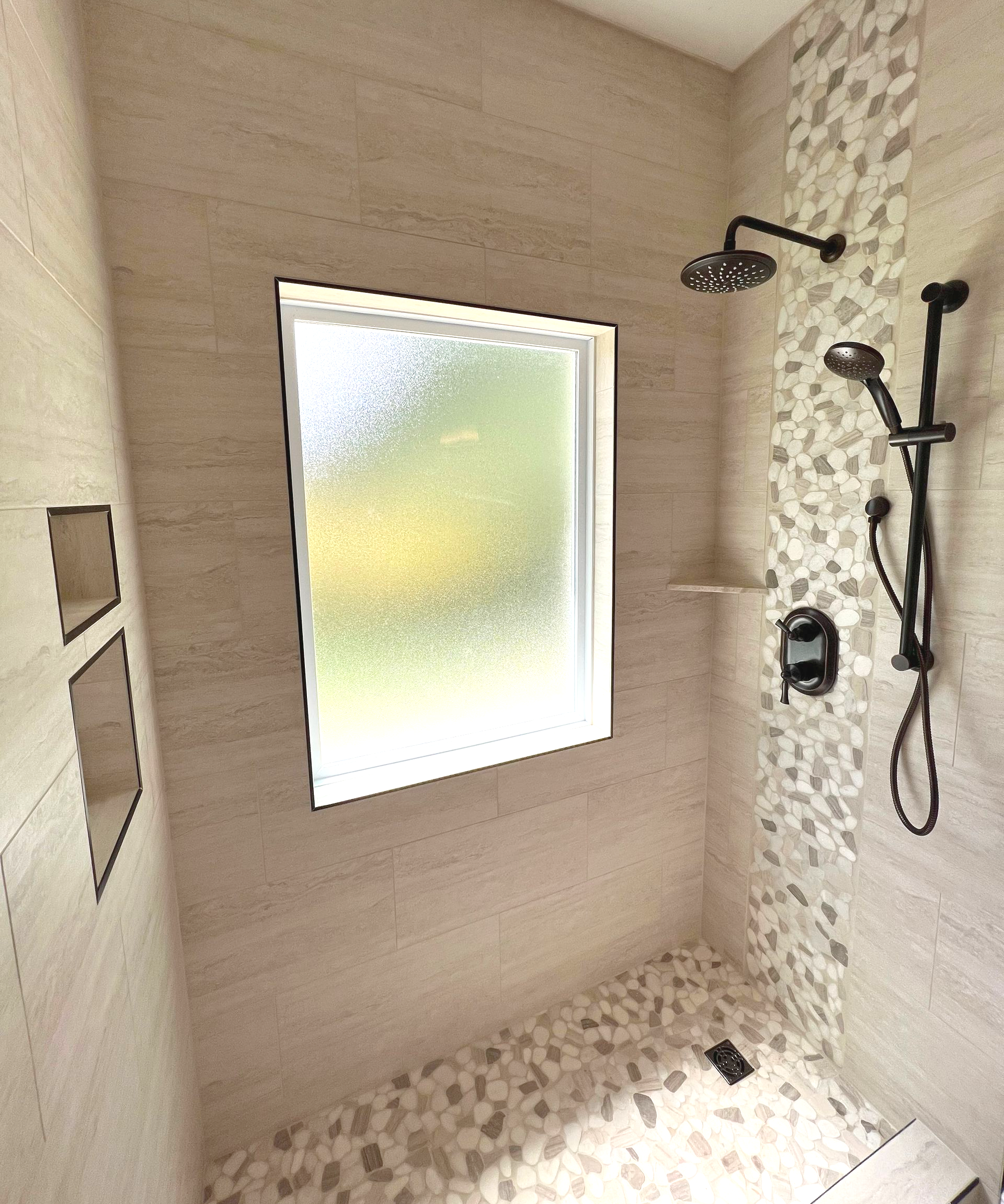 Modern tiled shower with frosted window, rainfall showerhead, handheld sprayer, and built-in shelf.