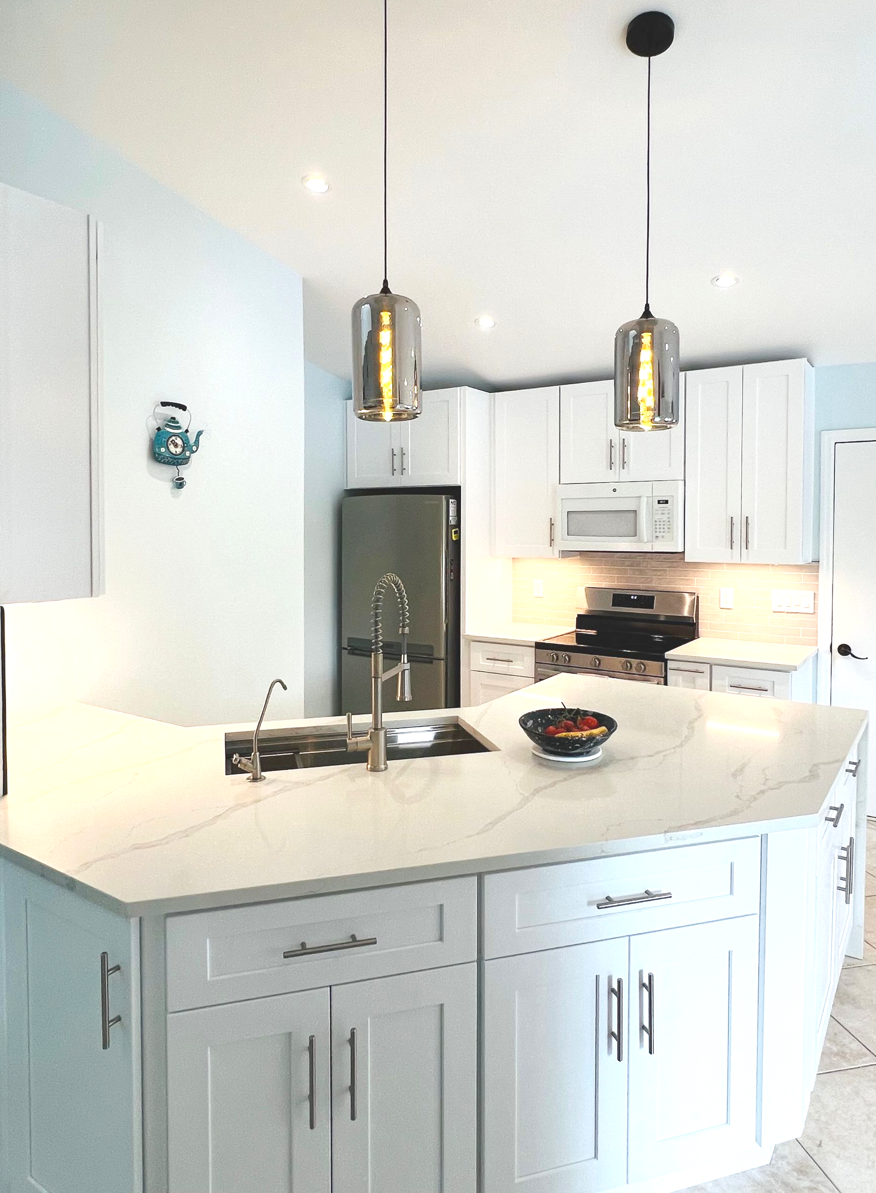 Bright modern kitchen with white cabinets, island, pendant lights, and stainless steel refrigerator.
