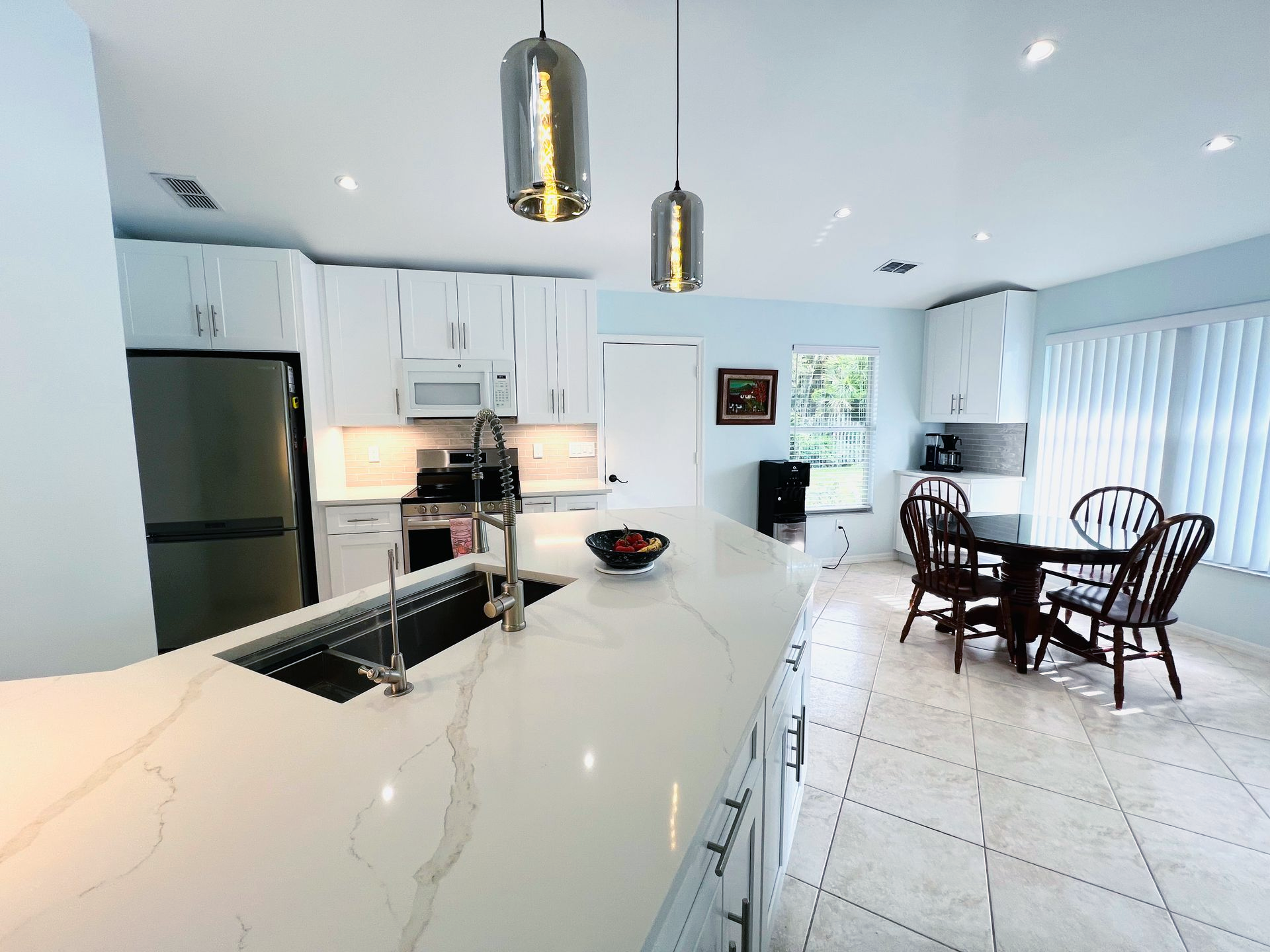 Bright white modern kitchen with island, black stools, stainless fridge, and dining table by sliding glass doors