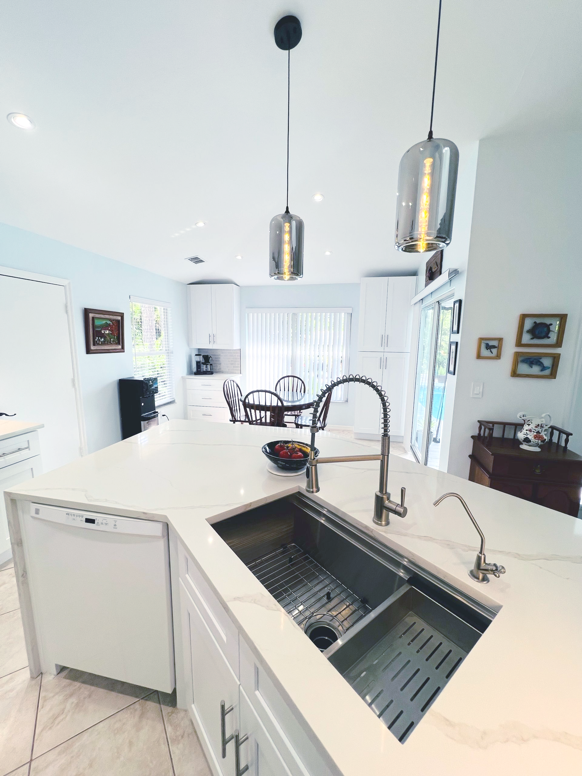 Bright white kitchen with island sink, pendant lights, and dining area in the background