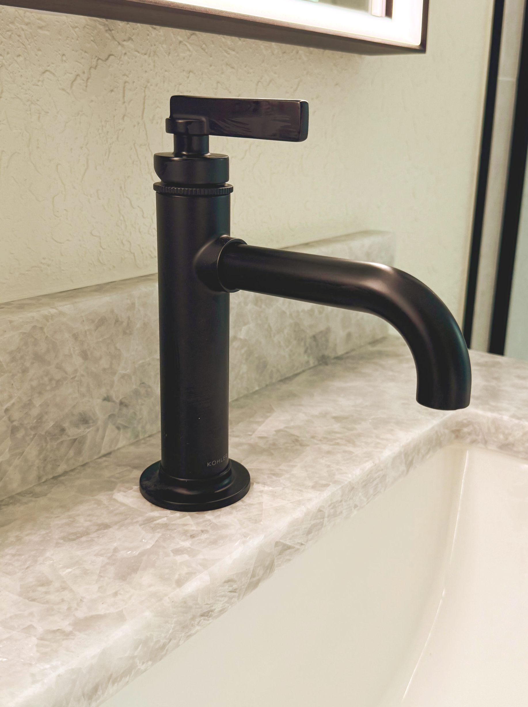 Black bathroom faucet mounted on a marble countertop beside a sink
