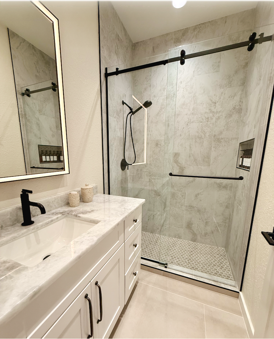 Modern white bathroom with black fixtures, vanity sink, mirror, and glass walk-in shower.