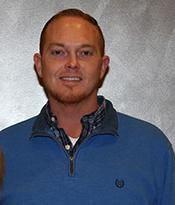 Man in a blue pullover standing against a gray textured backdrop