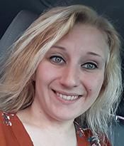 Smiling blonde person in a red patterned top inside a car