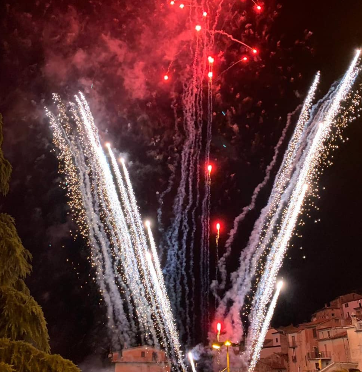 Spettacolo pirotecnico nel cielo notturno, con esplosioni rosse e bianche e scintille che si susseguono.