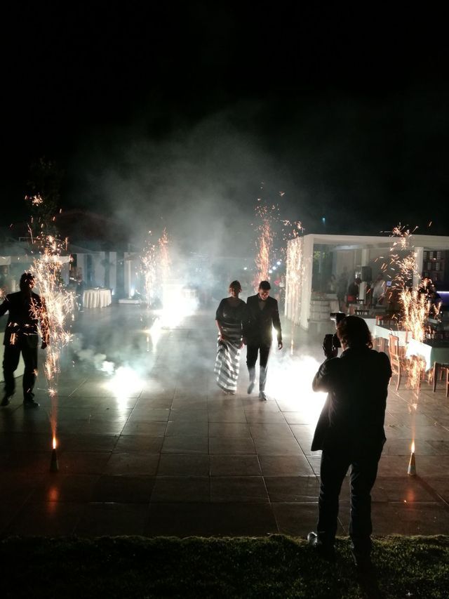 Due persone che camminano tra le stelle filanti di notte, mentre vengono fotografate. Fumo e ambiente buio.