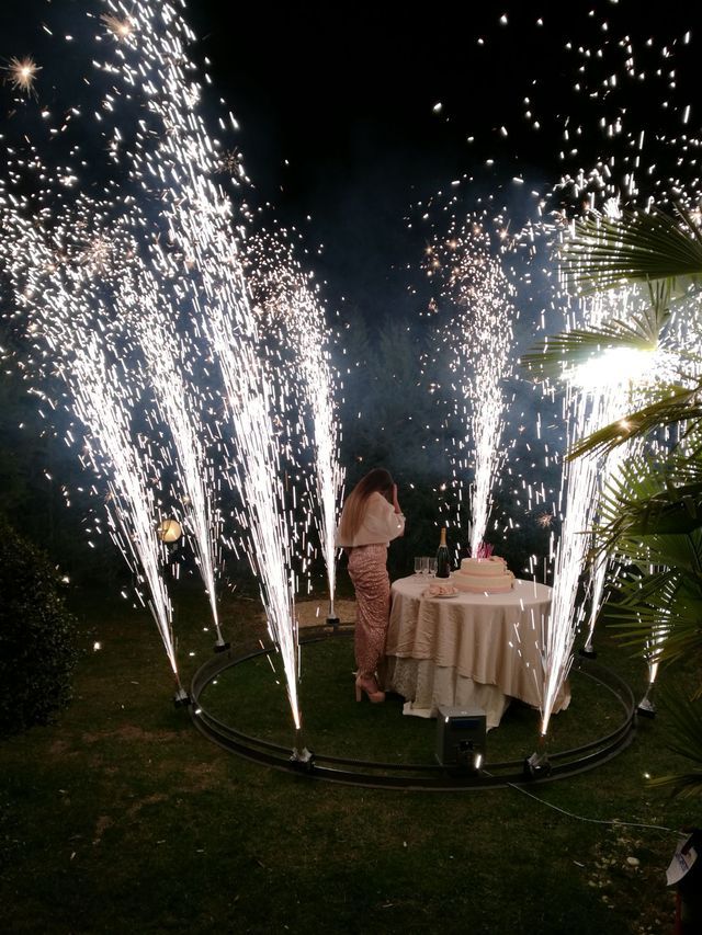 Donna vicino a una torta, circondata da fontane di scintille bianche, all'aperto di notte.