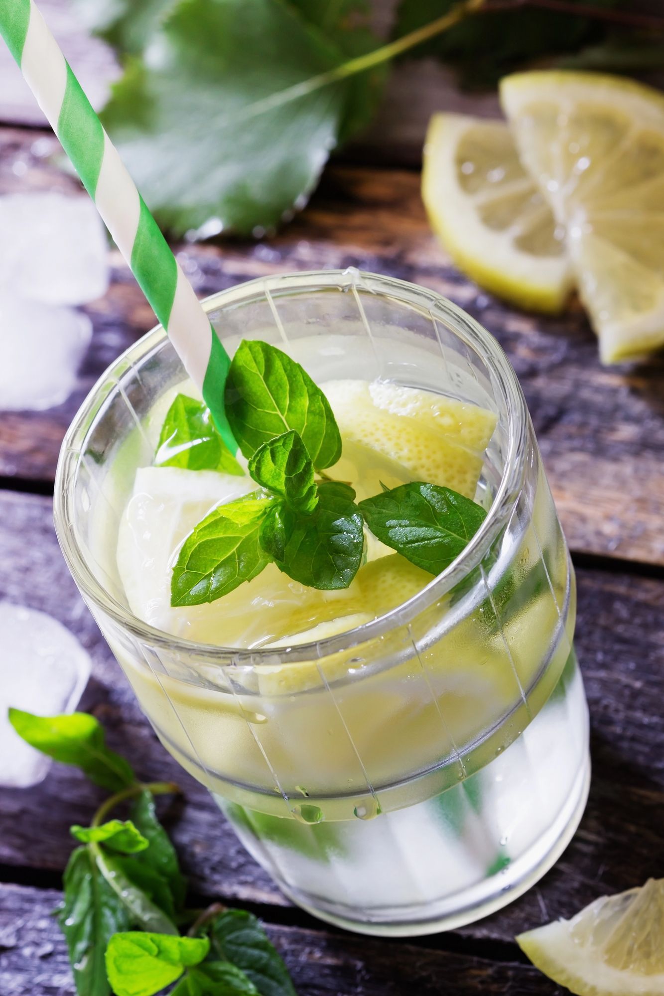 Limonata in un barattolo di vetro con foglie di menta e cannuccia a righe su un tavolo di legno rustico.
