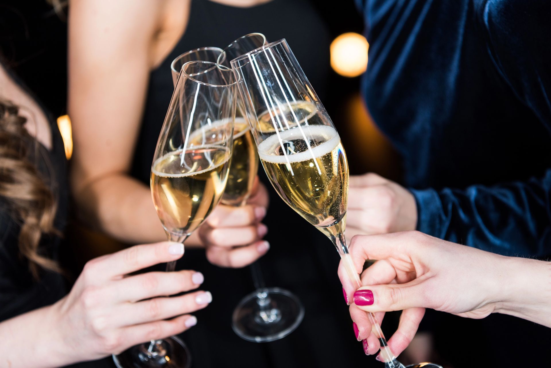 Mani che brindano con calici di champagne durante una festa, con spumante in un'atmosfera soffusa.
