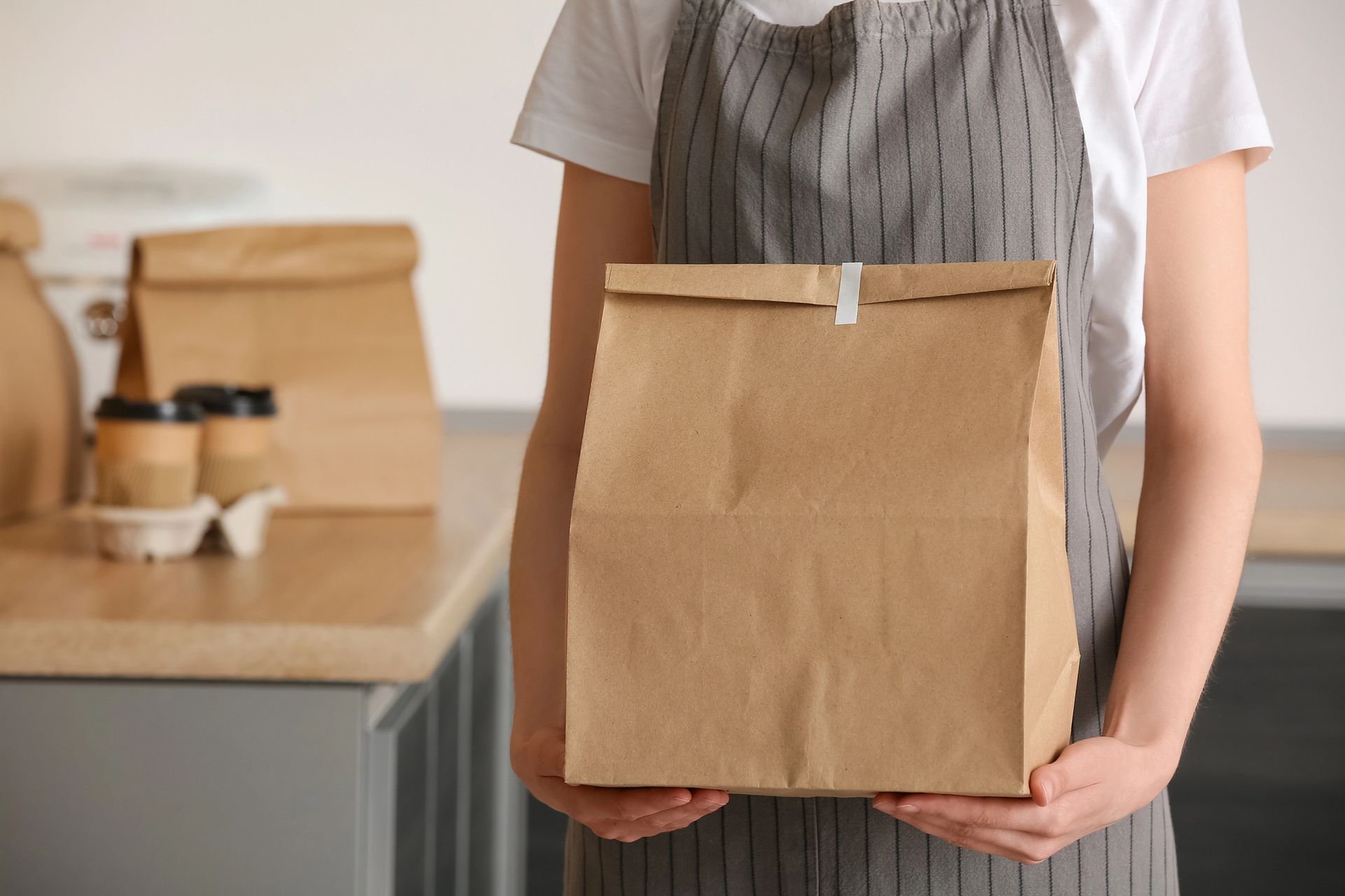 Persona che tiene in mano un sacchetto di carta marrone in un ambiente di cucina.