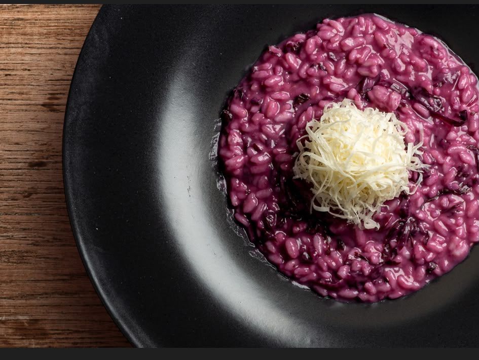 Risotto di barbabietola viola su un piatto nero con una montagna di formaggio grattugiato sopra.