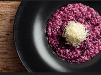 Risotto di barbabietola viola su un piatto nero con una montagna di formaggio grattugiato sopra.