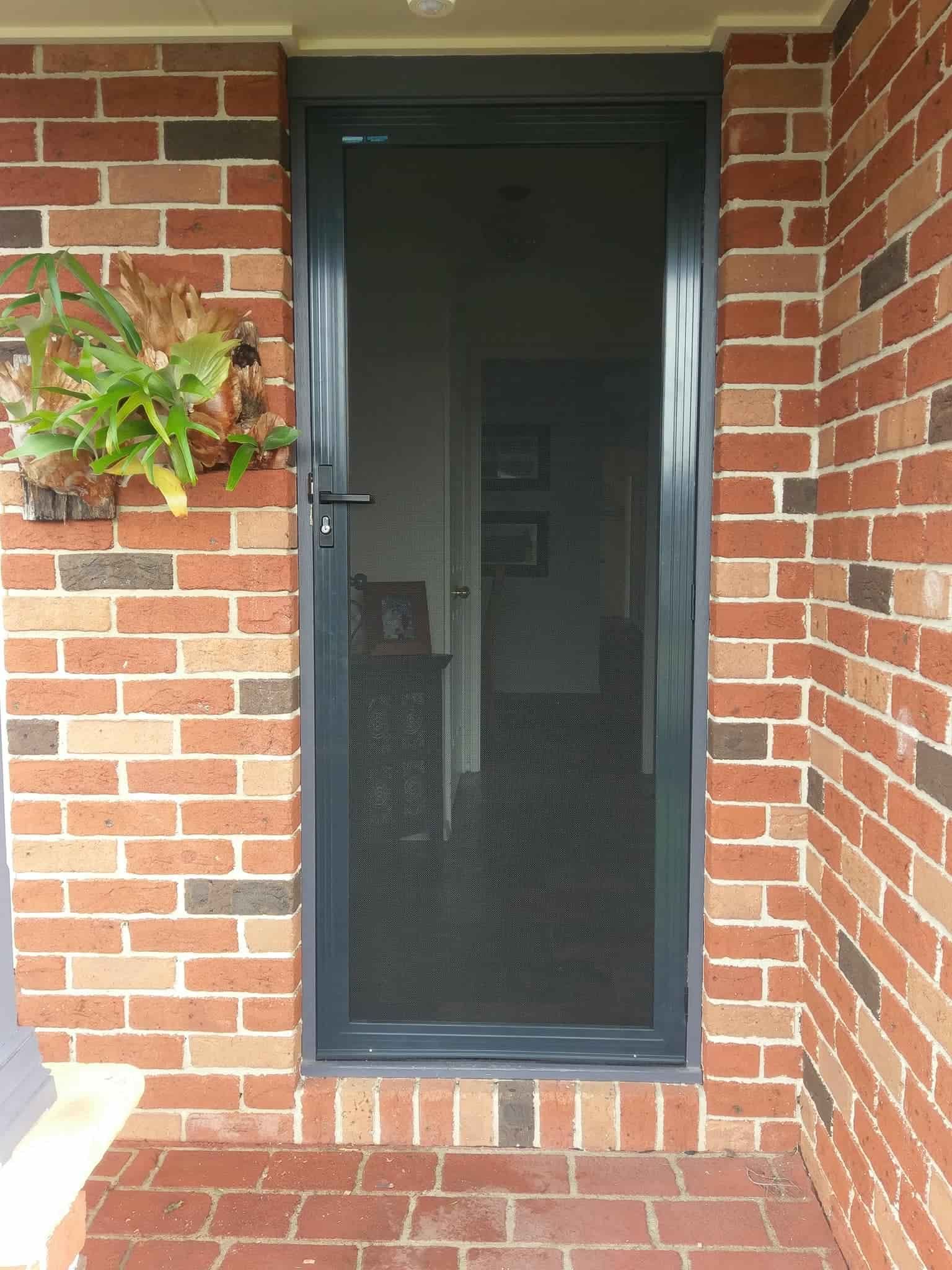 Grey security screen door in brick doorway, with a hanging plant to the left — Everything Screendoors & More In Wollongong, NSW