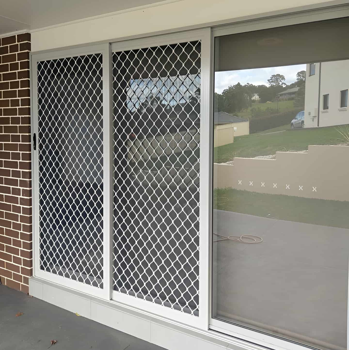 Sliding glass door with metal security screen; view of residential building, green grass, and trees — Everything Screendoors & More In Wollongong, NSW