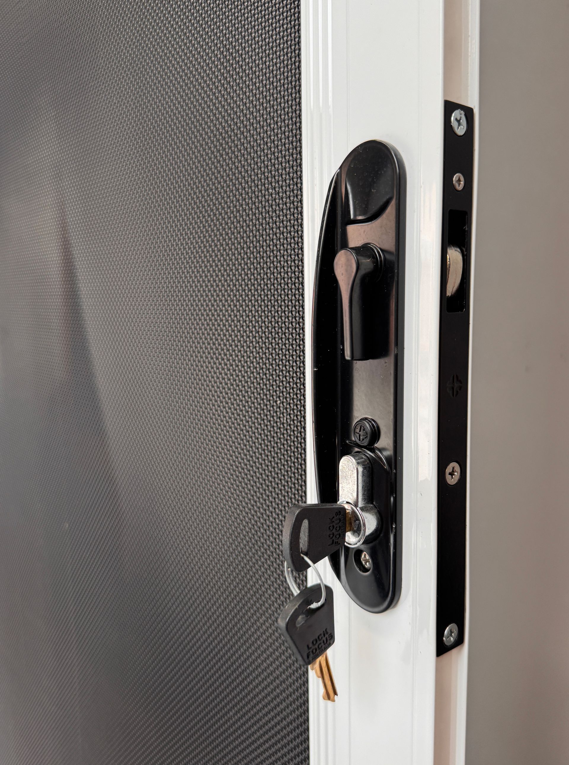 Black key in a door lock on a screen door, white frame, black strike plate — Everything Screendoors & More In Wollongong, NSW