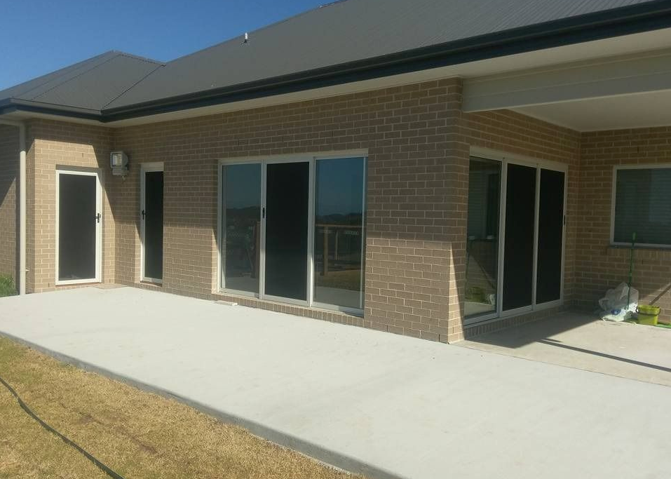 A brick home exterior with a concrete patio, sliding glass doors, and a lawn — Everything Screendoors & More In Wollongong, NSW