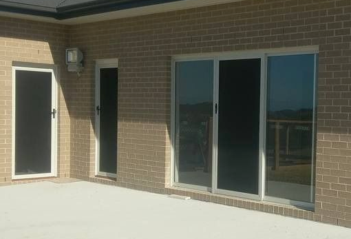 Brick house exterior with a concrete patio, featuring sliding glass doors and a screened door — Everything Screendoors & More In Wollongong, NSW