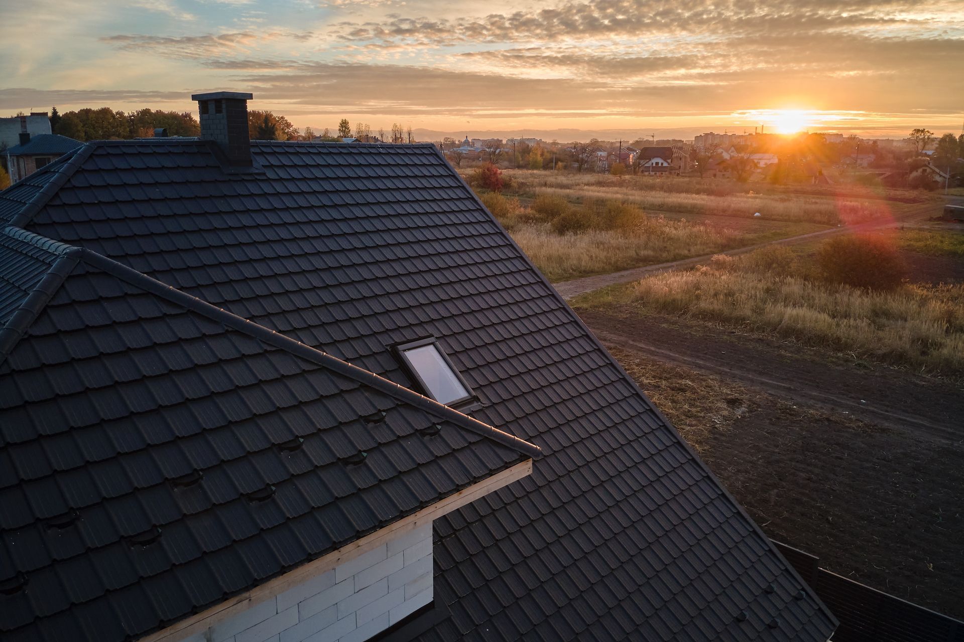 Dark Grey Tiled Roof With a Skylight and Chimney at Sunset — JLH Plumbing, Gas & Roofing in Wollongong, NSW