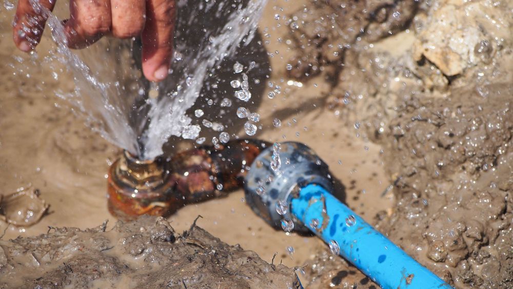 Person's Hand Near a Broken Pipe Spewing Water — JLH Plumbing, Gas & Roofing in Ulladulla, NSW