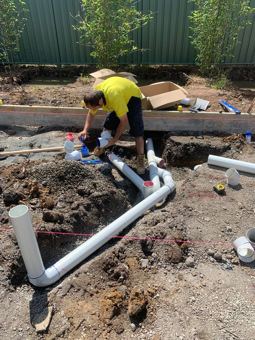 Man in Yellow Shirt Connects Pvc Pipes in a Dirt Excavation — JLH Plumbing, Gas & Roofing in South Nowra, NSW