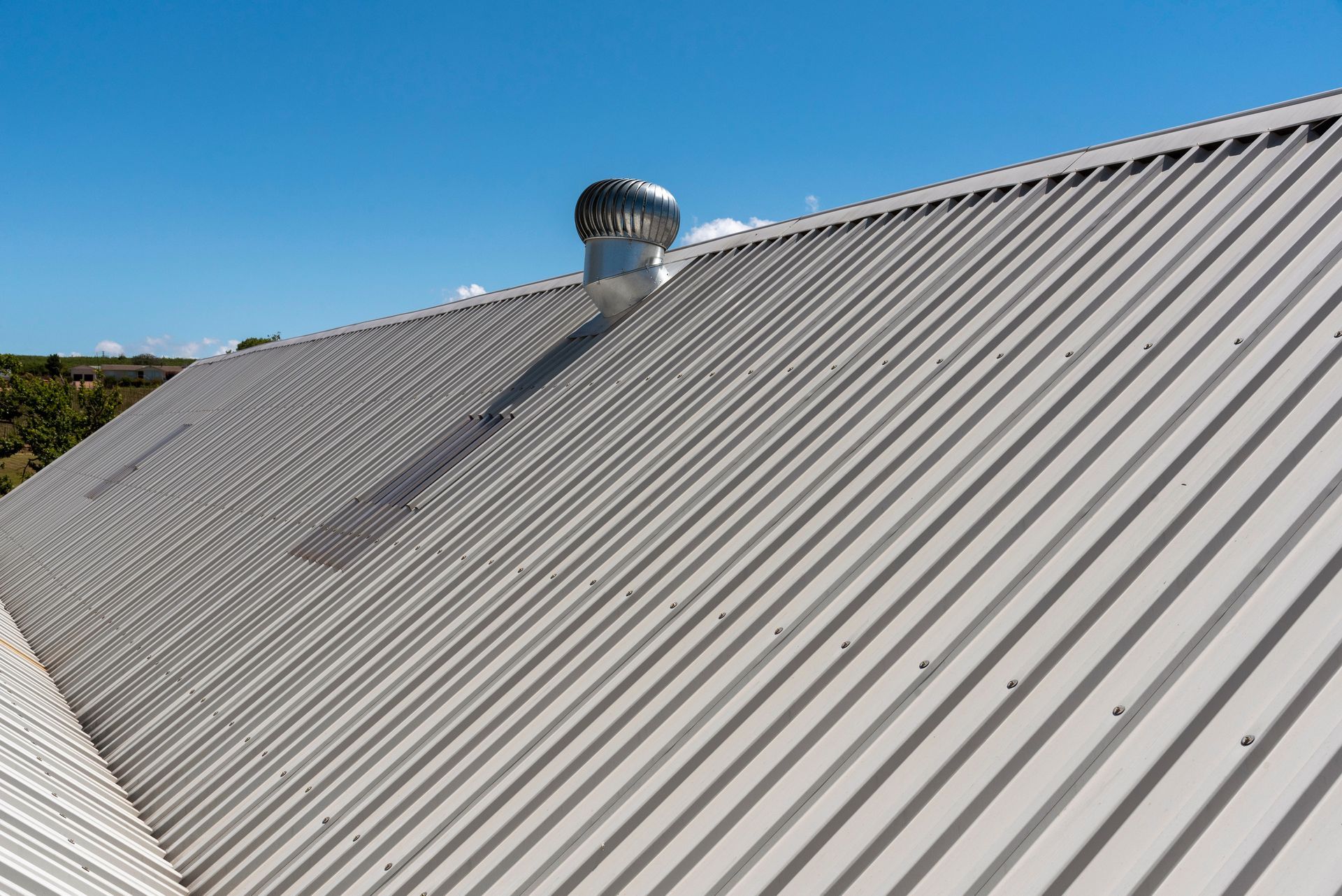 Corrugated metal roof with a rotating vent against a bright blue sky — JLH Plumbing, Gas & Roofing in South Nowra, NSW