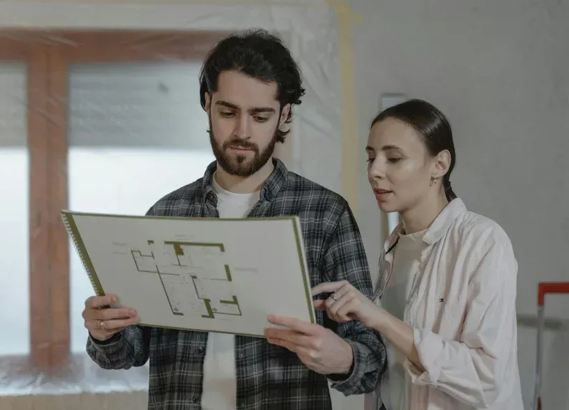 Due persone esaminano una planimetria in una stanza luminosa, indicando insieme il disegno.