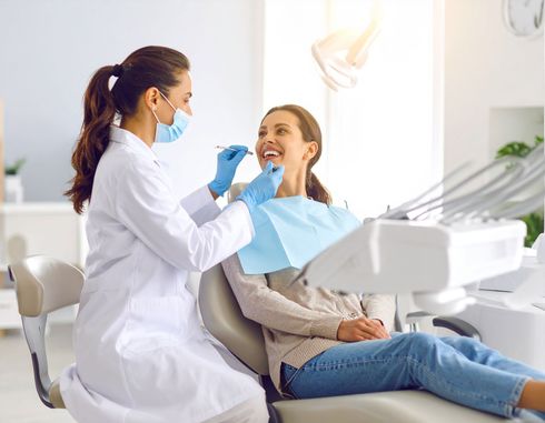 Dentist examining a smiling patient's teeth in a bright dental office.