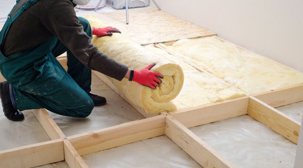 A Man is Rolling a Roll of Insulation on a Floor — Fullerton's Plumbing Manufacture In Woree, QLD