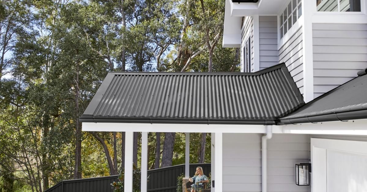 Gray home with black corrugated metal roof and white pillars.