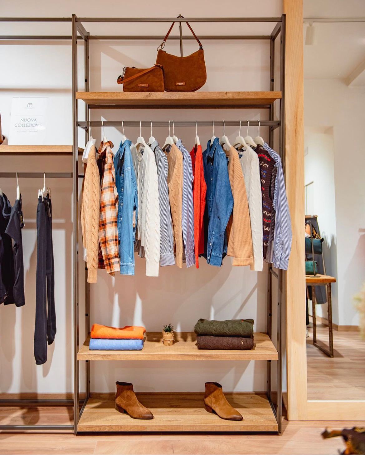 Clothing rack with colorful shirts, folded sweaters, boots, and a brown handbag in a boutique shop