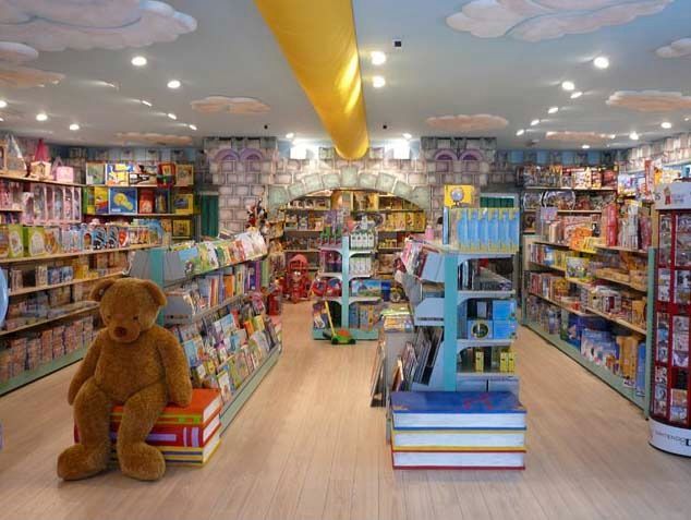 Bright children’s bookstore aisle with colorful shelves, a large teddy bear, and a cloud-painted ceiling