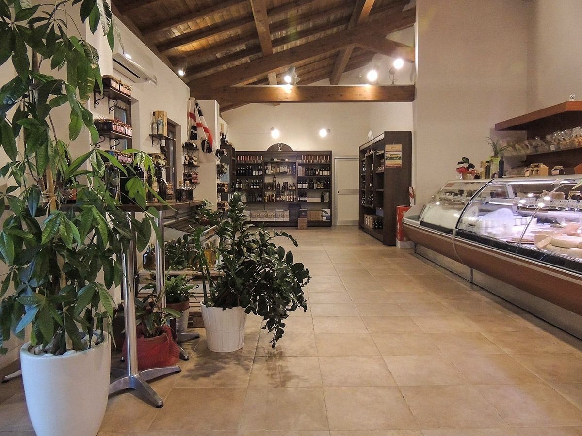 Interior of a small market or deli with shelves, potted plants, and a long refrigerated display case.