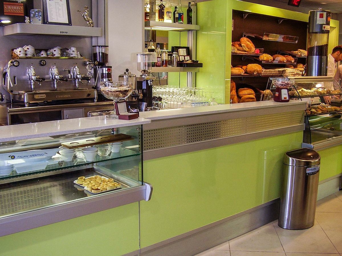 Cafe counter with espresso machines, glass pastry case, and baked goods on shelves behind it