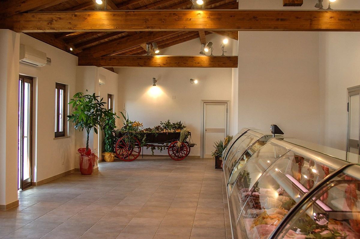 Spacious café or market interior with wooden beams, potted plants, and a curved glass display case.