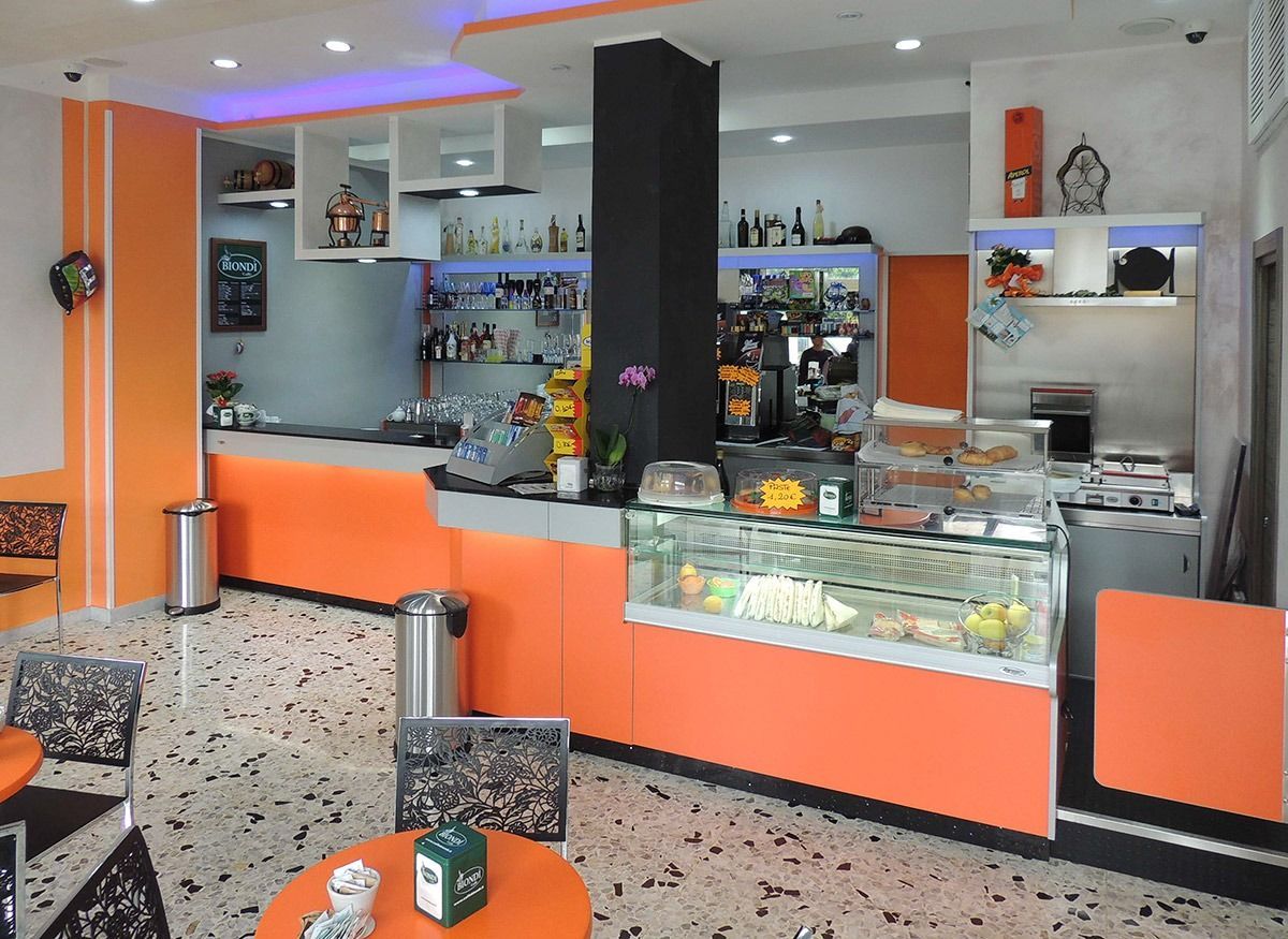 Empty café counter with orange panels, glass display case, and stools in a bright modern interior