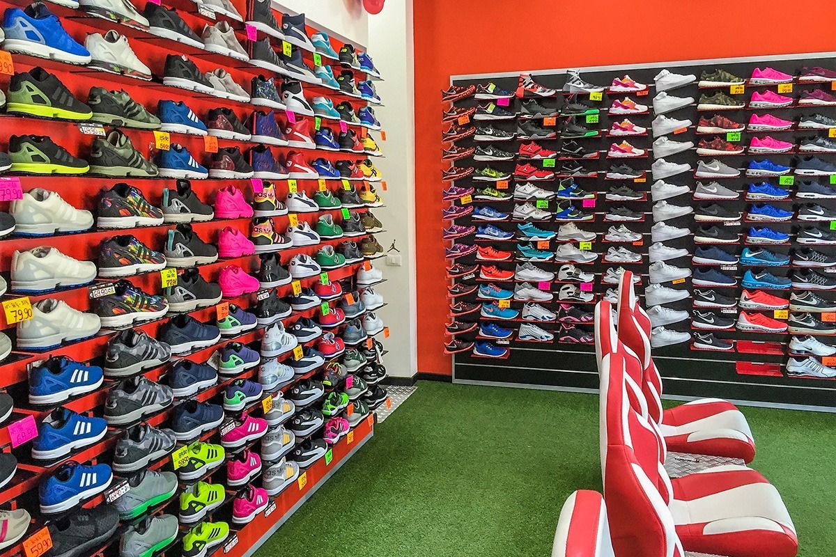 Shoe store aisle with colorful athletic shoes lined on wall shelves and white-and-red chairs on green carpet
