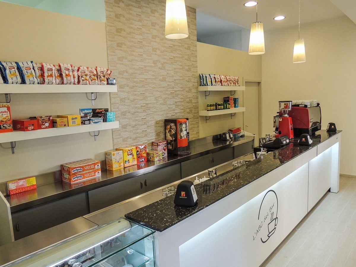 Bright café counter with shelves of snacks, pendant lights, and coffee machines on a clean beige wall