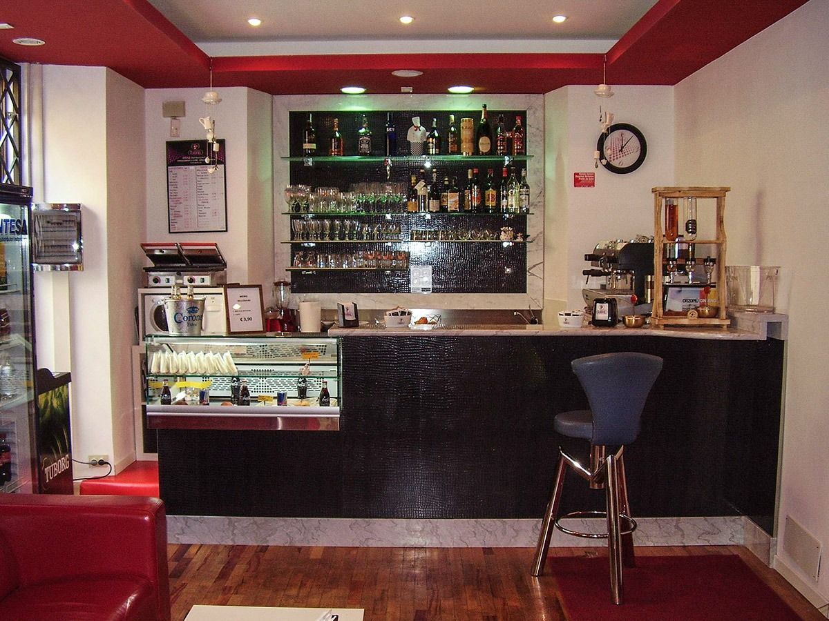 Small bar interior with red ceiling, dark counter, shelves of bottles, and a stool at the bar.