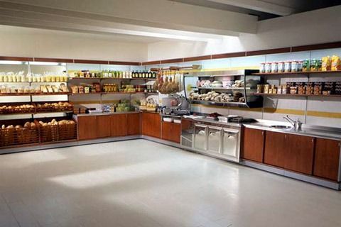 Empty cafeteria counter with stainless steel serving stations and shelves of drinks and food items