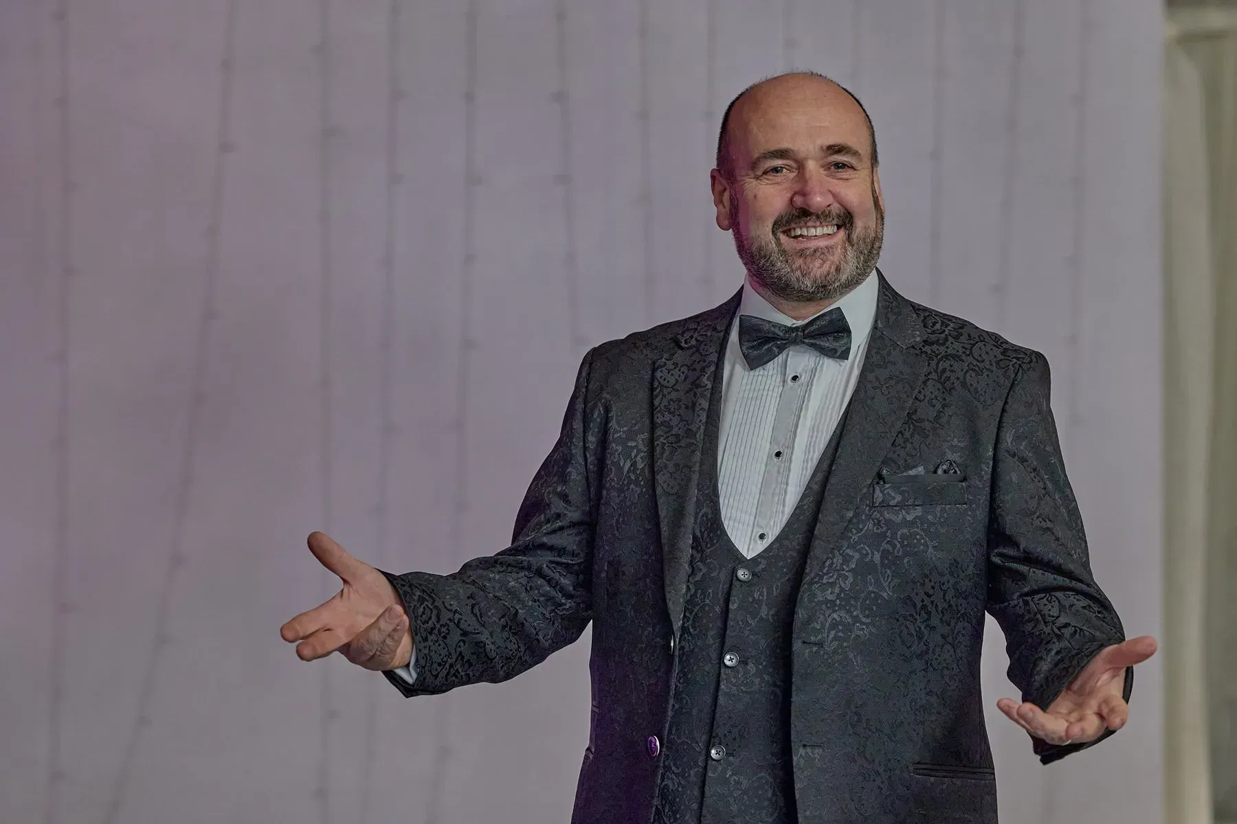 A man in a suit and bow tie is standing with his arms outstretched.